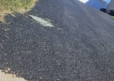 A freshly paved driveway with a small patch of grass and a white fence in the background.