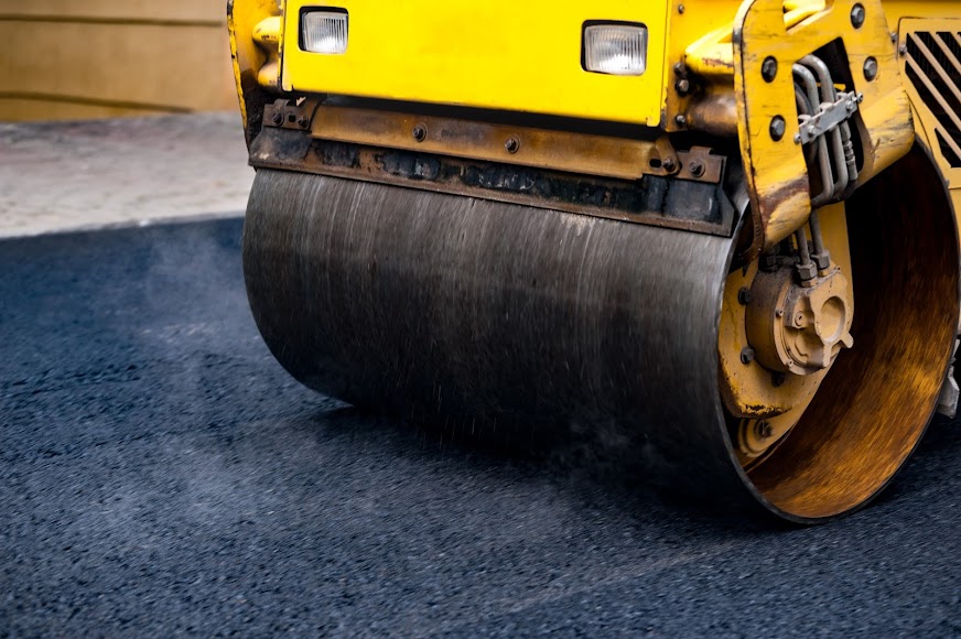 download-15 Close-up of a yellow steamroller compacting fresh asphalt on a road.