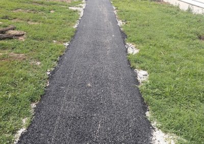 Freshly paved asphalt walkway curves through grass toward a road, with houses visible in the background.