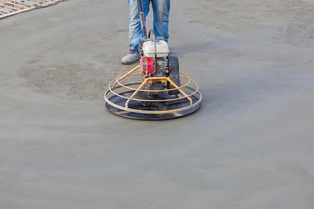 Worker using a power trowel to smooth freshly poured concrete on a construction site.