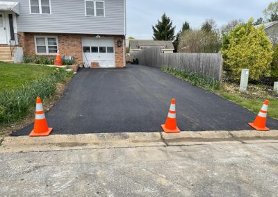 Freshly paved driveway with three orange traffic cones at the entrance to block access.