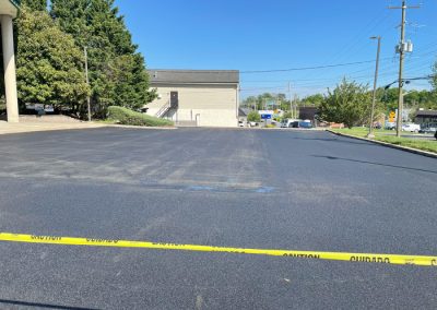 Freshly paved parking lot blocked off with yellow caution tape on a sunny day.