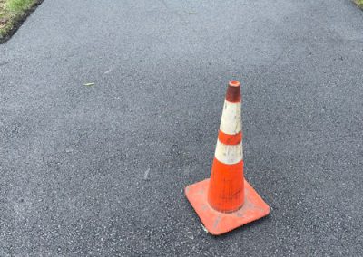 An orange traffic cone sits on a newly paved driveway, blocking entry.