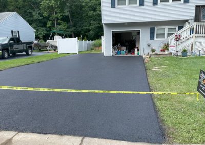 Freshly paved blacktop driveway in front of a house, blocked by yellow caution tape.