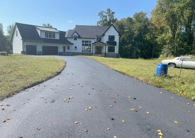 A modern house with a black driveway, grassy lawn, and a white car parked on the right.