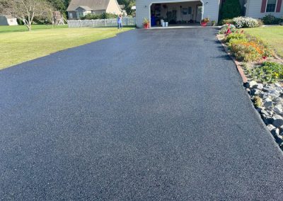 Freshly paved asphalt driveway leading to a garage, with flowers and grass bordering the edges.