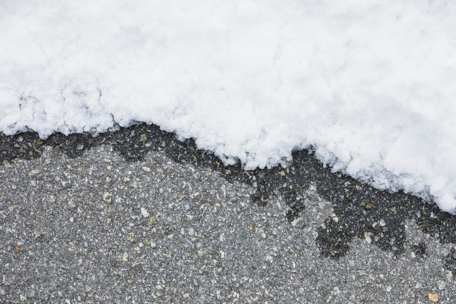 2147963630 A layer of snow partially covering a section of gray asphalt pavement.